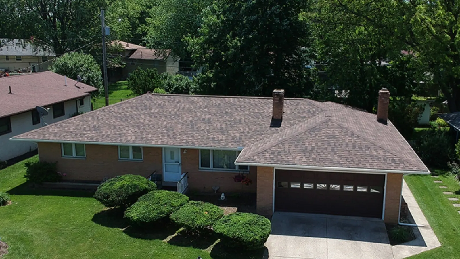 Aerial view of a brick ranch home with a completed architectural shingle roof and attached garage