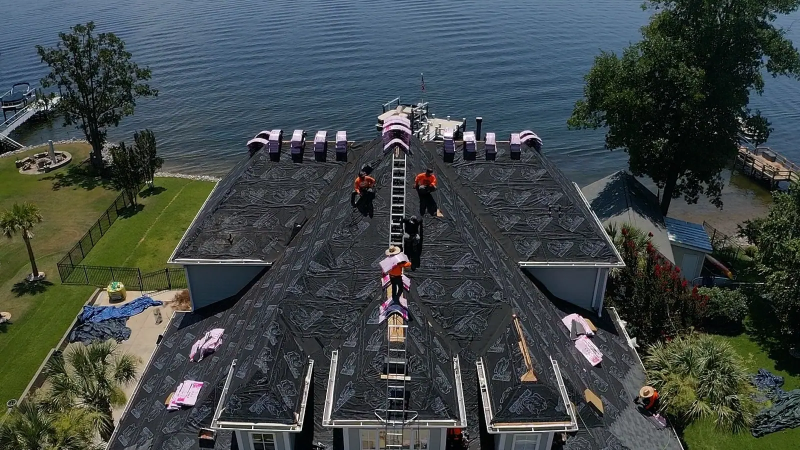 Roof replacement in progress on a long lakefront home with new bundles staged along the ridge