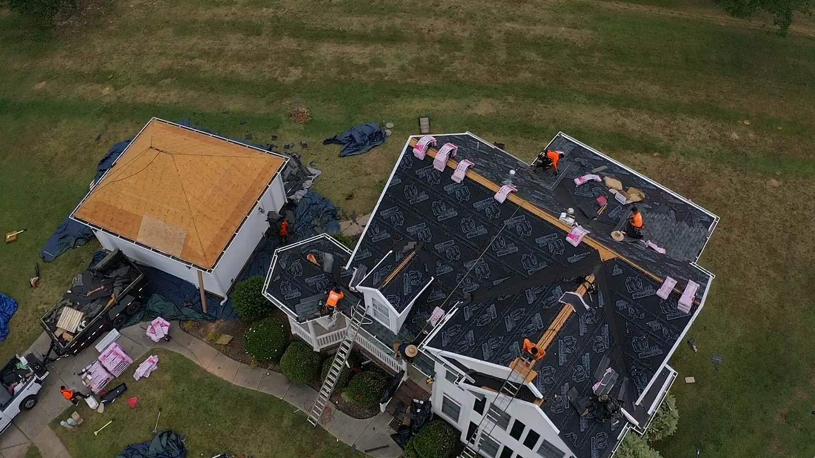 Aerial view of a roof replacement underway with landscaping tarped off below the work area